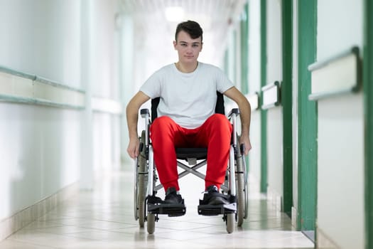 Young teenage boy smiling while sitting in a wheelchair in a hospital hallway. Rehabilitation and positivity concept