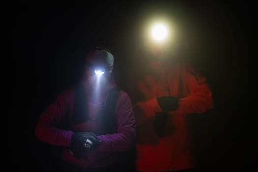 Couple equipped with headlamps explore a forest in total darkness, with beams of light cutting through the night air.