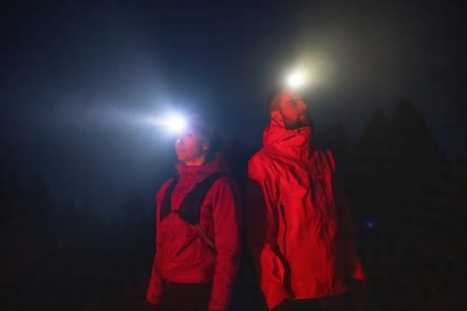 Couple equipped with headlamps explore a forest in total darkness, with beams of light cutting through the night air.