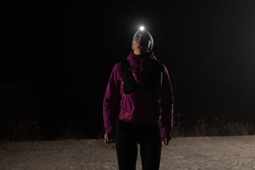 Woman jogging at night with headlamp on, captured in dark outdoor environment.