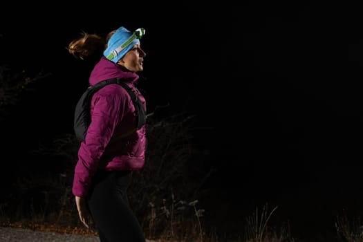 Woman jogging at night with headlamp on, captured in dark outdoor environment.