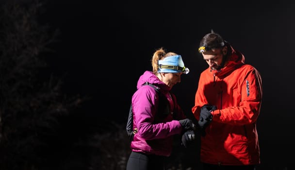 Couple night hikers examine a device under headlamp light, emphasizing navigation and teamwork under low light conditions.