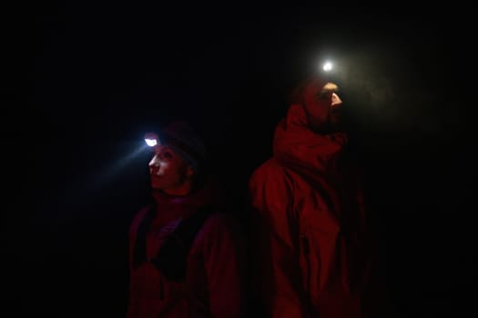 Couple equipped with headlamps explore a forest in total darkness, with beams of light cutting through the night air.