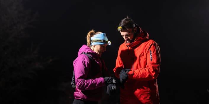 Couple night hikers examine a device under headlamp light, emphasizing navigation and teamwork under low light conditions.