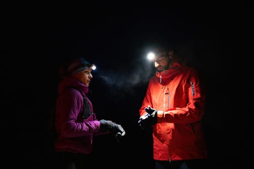 Couple night hikers examine a device under headlamp light, emphasizing navigation and teamwork under low light conditions.