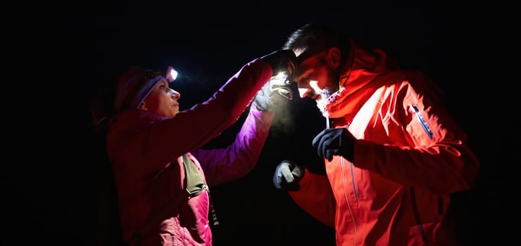 A woman provides headlamp-assisted first aid to a man outdoors in the dark, showcasing emergency preparedness in extreme conditions.