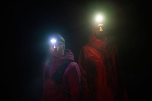Couple equipped with headlamps explore a forest in total darkness, with beams of light cutting through the night air.