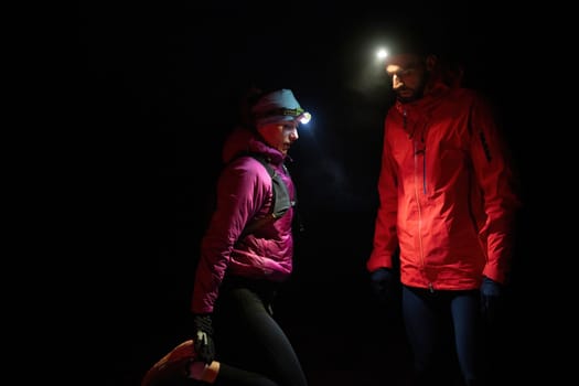 Couple equipped with headlamps explore a forest in total darkness, with beams of light cutting through the night air.
