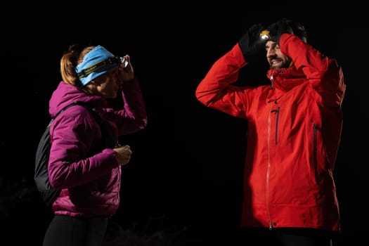 Couple equipped with headlamps explore a forest in total darkness, with beams of light cutting through the night air.
