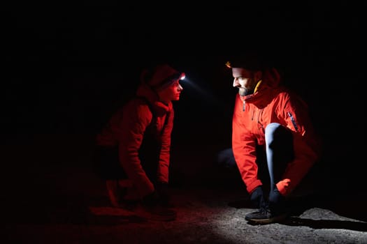 Two trekkers inspect their shoes using headlamps during a night hike, emphasizing safety and preparation in the dark.