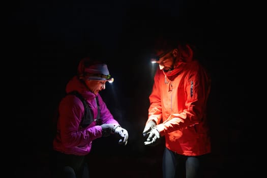 Couple night hikers examine a device under headlamp light, emphasizing navigation and teamwork under low light conditions.