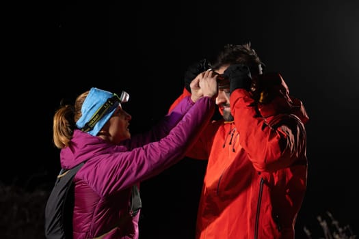 A woman provides headlamp-assisted first aid to a man outdoors in the dark, showcasing emergency preparedness in extreme conditions.