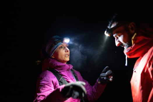 A woman provides headlamp-assisted first aid to a man outdoors in the dark, showcasing emergency preparedness in extreme conditions.