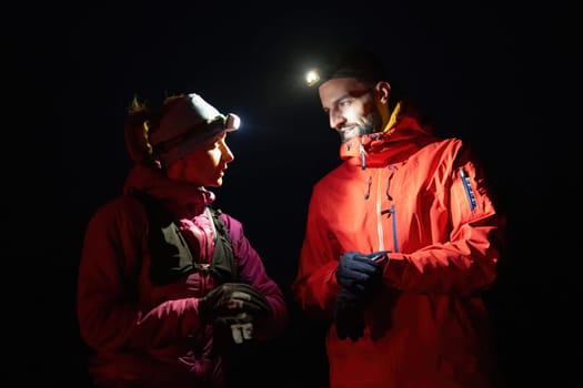 Couple night hikers examine a device under headlamp light, emphasizing navigation and teamwork under low light conditions.