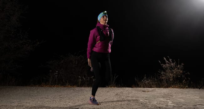 Woman jogging at night with headlamp on, captured in dark outdoor environment.
