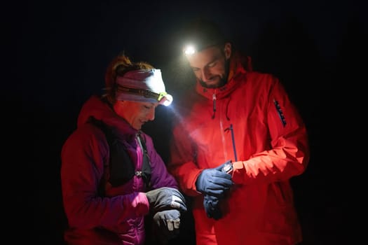 Couple night hikers examine a device under headlamp light, emphasizing navigation and teamwork under low light conditions.