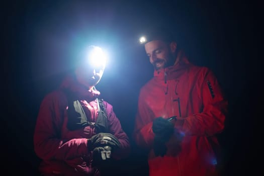 Couple night hikers examine a device under headlamp light, emphasizing navigation and teamwork under low light conditions.
