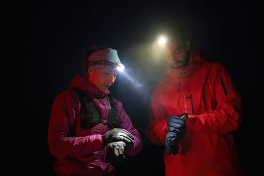 Couple night hikers examine a device under headlamp light, emphasizing navigation and teamwork under low light conditions.