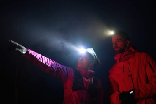 A woman points into the distance while discussing directions with her hiking partner under the beam of headlamps