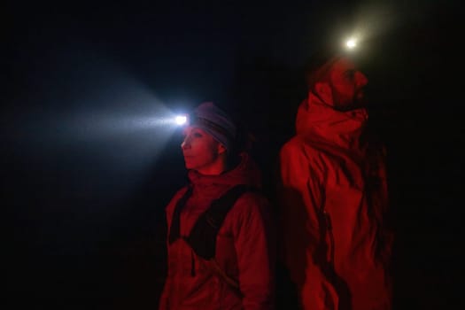 Couple equipped with headlamps explore a forest in total darkness, with beams of light cutting through the night air.