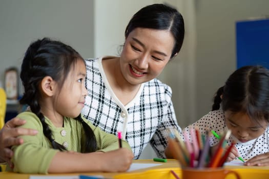 A teacher interacts warmly with young students as they enjoy a creative drawing session, fostering a love for learning.