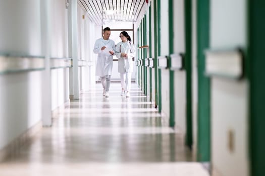 Two doctors in white coats walking and discussing medical documents in a brightly lit hospital corridor, emphasizing teamwork and professional healthcare environment.