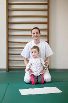 Female physiotherapist helping a young child with physical exercises in a rehabilitation center. Pediatric therapy and development concept.