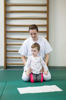 Female physiotherapist helping a young child with physical exercises in a rehabilitation center. Pediatric therapy and development concept.