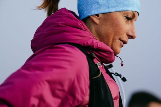 A woman athlete running along a rocky mountain trail in cold, misty weather, wearing a warm jacket, gloves, and a headband, showcasing endurance and determination.