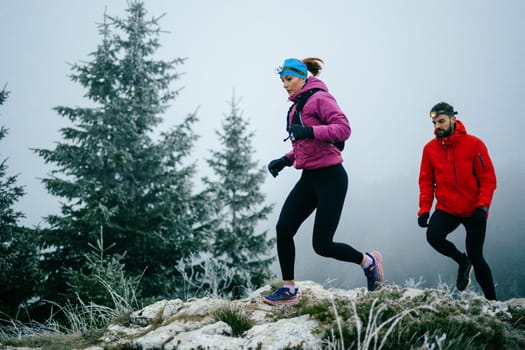 Trail running couple man and woman running on a mountain path. A couple on cross country run in early morning.