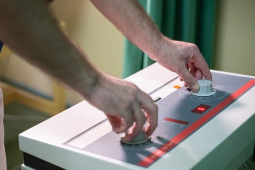 Close up of hands adjusting settings on a physiotherapy device used for therapeutic treatment in a clinic.