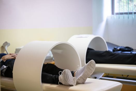 Patients lying down with legs inside circular magnetic therapy devices during a physiotherapy session.