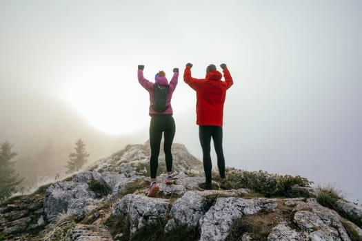 Two Hikers Celebrating on Rocky Peak.Couple hikers raising fists on rugged mountain ridge at sunrise