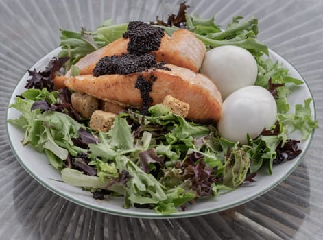 Homemade salad with Grilled salmon fillets, Boiled egg and Croutons topping Caviar on plate. Simple yet very tasty dish, use it as your Wallpaper, Poster and Space for text, Selective focus.