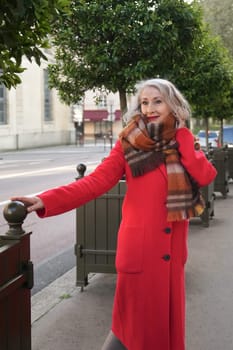 Gray-haired woman of sixty years old in a red coat and a terracotta scarf walking in the city