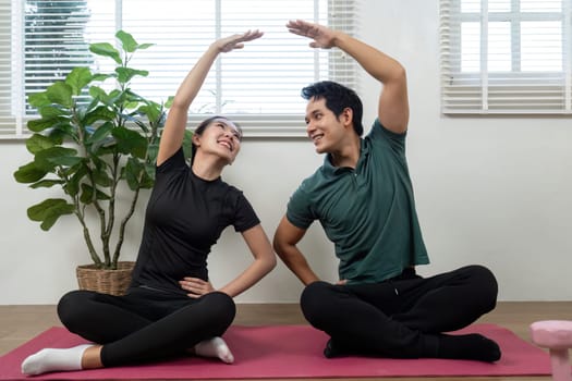 A couple happily performing stretching exercises, promoting wellness and emotional connection in a warm home atmosphere.
