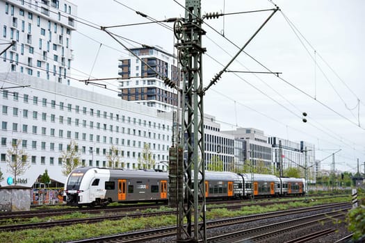 Dusseldorf, Germany 05.22.2025 Double decker commuter train rides along electrified railway tracks with contemporary high rise buildings in the background on a cloudy day