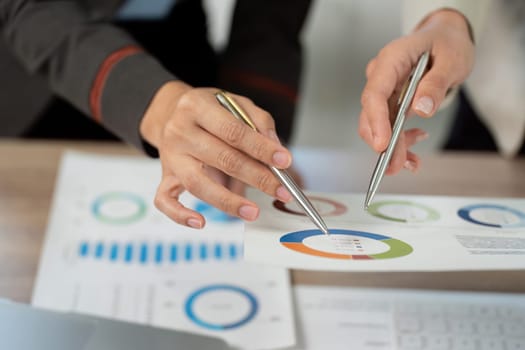 Close-up of hands pointing at data charts and reports, illustrating teamwork and analysis in a business environment.