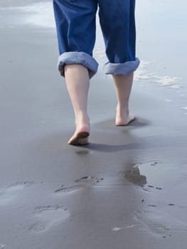 A closeup conceptual photos of a woman's feet shown barefooted walking on the beach by the pacific ocean in Washington.