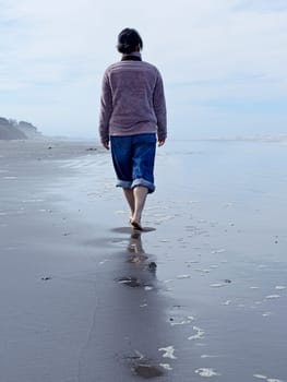 A woman walks barefooted on the beach on a sunny day along the coast of Washington State.