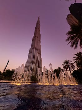 UAE, Dubai, 19 September 2024: The famous Burj Khalifa skyscraper at dusk, fountain, Dubai's sights during the incredible sunset sky, skyscrapers illuminated at night, pink sky, palm trees. High quality photo