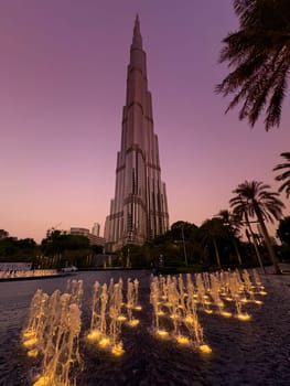 UAE, Dubai, 19 September 2024: The famous Burj Khalifa skyscraper at dusk, fountain, Dubai's sights during the incredible sunset sky, skyscrapers illuminated at night, pink sky, palm trees. High quality photo