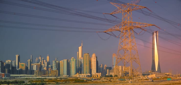Dubai's high-voltage power lines at sunset, skyscrapers in the haze in the background. High quality photo
