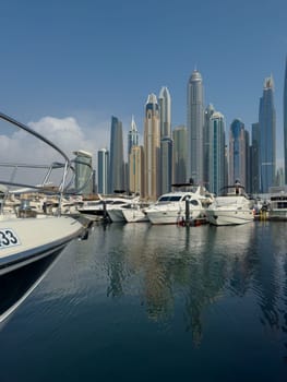 UAE, Dubai, 29 September 2024: Skyscrapers from Dubai harbor marina at sunny day, luxury yachts and boats are moored in port. High quality photo