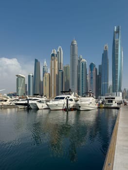 UAE, Dubai, 29 September 2024: Skyscrapers from Dubai harbor marina at sunny day, luxury yachts and boats are moored in port. High quality photo