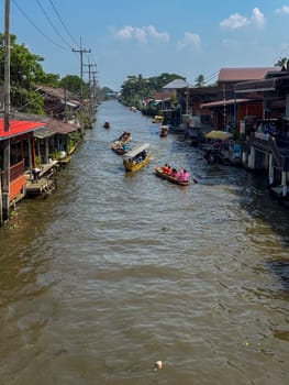 Bangkok, Thailand - November 12, 2024: Tourists shopping at a famous floating market in Bangkok, popular attraction where tourists explore a floating bazaar and enjoying Thai food from boat vendors.