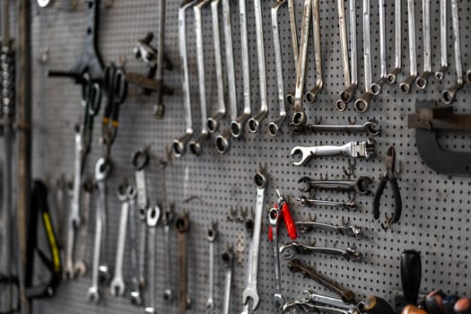 Various wrenches and hand tools hanging on pegboard in workshop. Neatly organized tools include combination wrenches, pliers, and adjustable wrenches for mechanical work