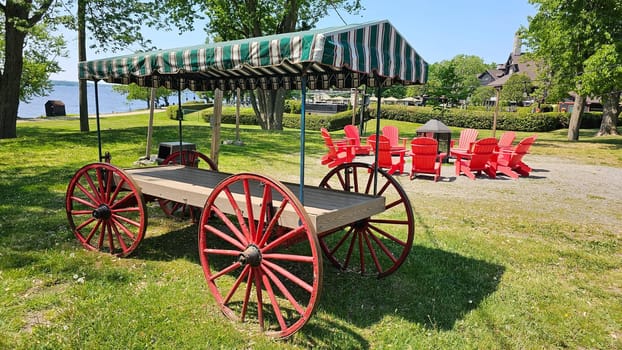 Ottawa, ON Canada - 06.04.2023: Vintage Wagon with Striped Canopy and Red Chairs in a Tranquil Lakeside Setting, Summer Day.
