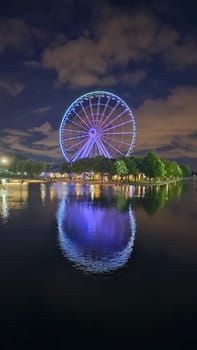 Montreal, QC Canada - 07.21.2023: Ferris Wheel at Night A Mesmerizing Reflection on Water, Illuminating the Dark Sky Landscape.