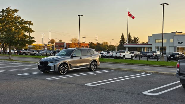 Ottawa, ON Canada - 10.04.2023: Silver BMW X5 SUV Parked in a Car Dealership Parking Lot on a Sunny Day, Canada Flag in Background.